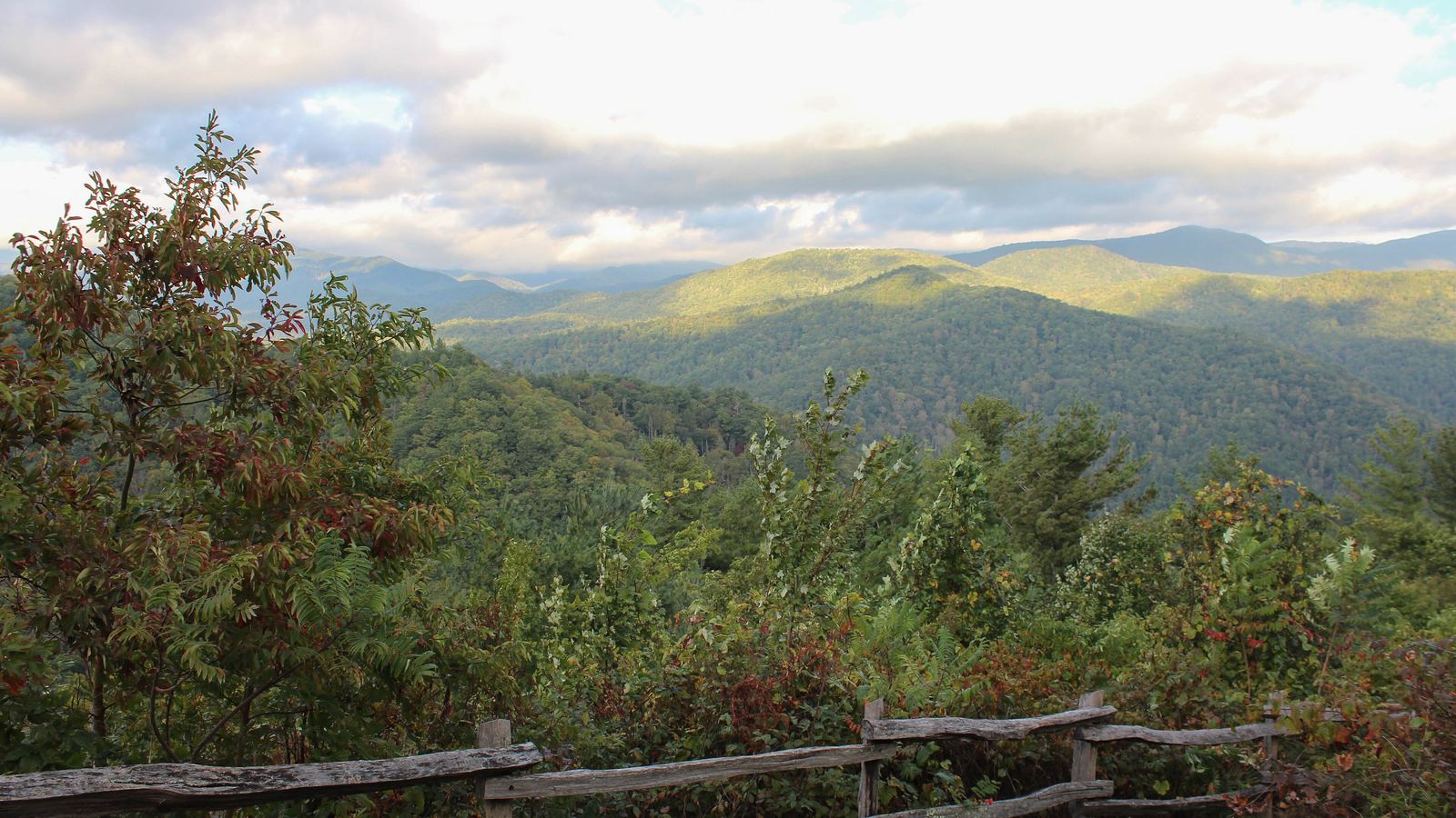 A split-rail fence at an overlook with layered green mountains beyond, in the Smokies