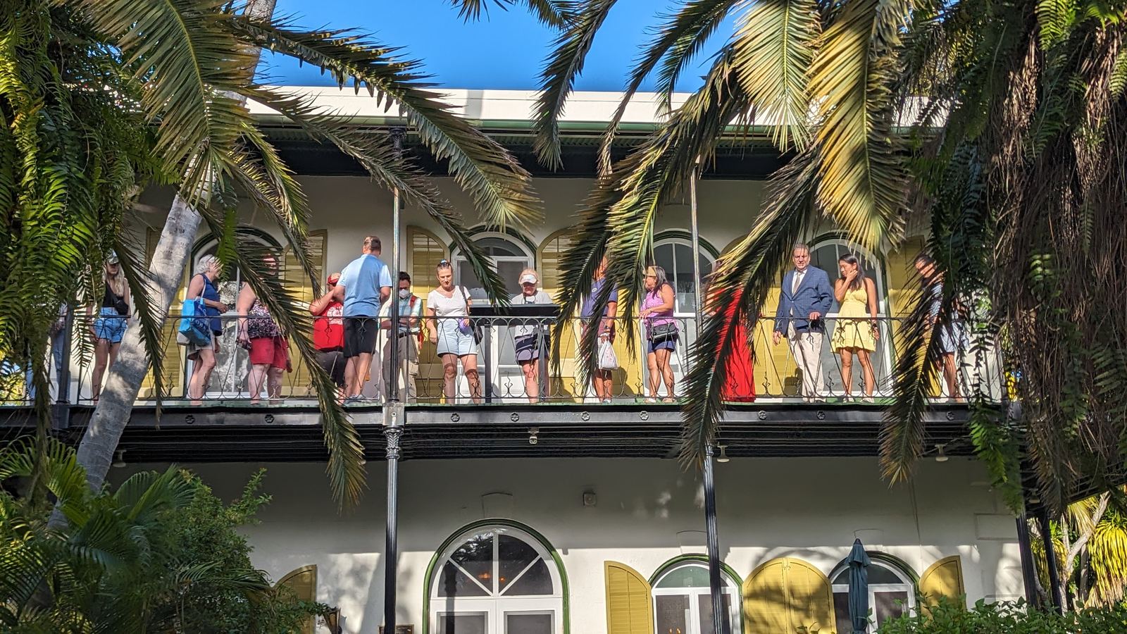 Visitors on the veranda of the Ernest Hemingway Home and Museum in Key West, framed by palms